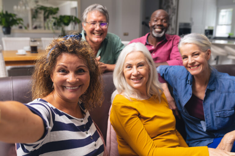 Cheerful multiracial senior male and female friends taking selfie together at home. unaltered, lifestyle, enjoyment, fun, friendship, wireless technology and togetherness.