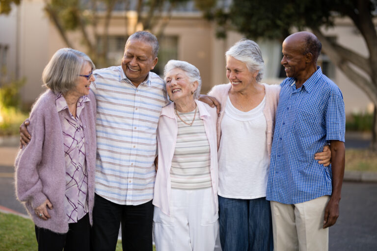 Smiling senior friends standing with arms around outside nursing home