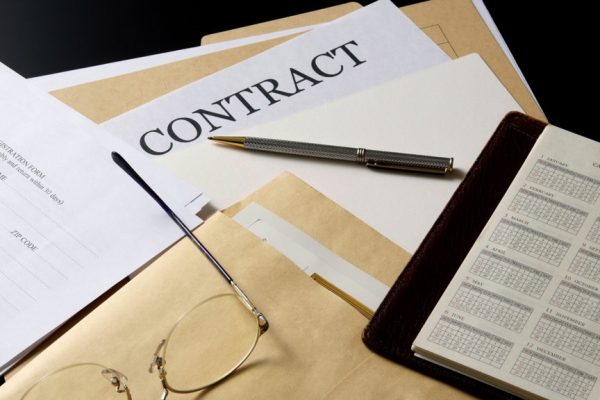 Stacked contract documents and personal organizer on the office desk.